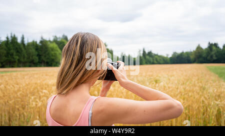 Ansicht von hinter der professionellen Fotografin Fotos, die in der Natur des schönen goldenen Sommer Felder. Stockfoto