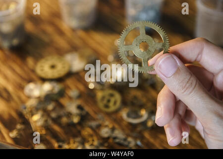 Watch Werkstatt hält große Zahnrad. Großes Metall Zahnrad auf unscharfen Arbeitsbereich. Zahnrad an verschwommenen Hintergrund der Arbeitsplatz. Ritzel in weiblicher Hand. Alten Cog Stockfoto