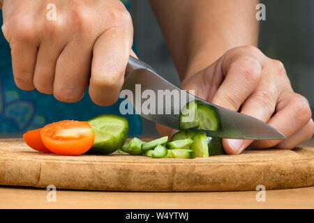 Hände von Frau hacken Gurken und Tomaten auf dem Schneidebrett für Salat, Nahaufnahme Stockfoto