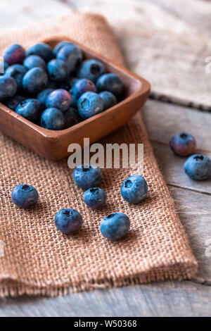 Heidelbeeren im Holz Schale auf der Oberseite von Sackleinen, mit einem hölzernen Tischplatte Stockfoto