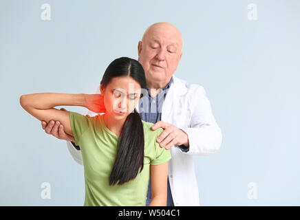 Leitender Physiotherapeut arbeiten mit jungen asiatischen Frau auf hellen Hintergrund Stockfoto