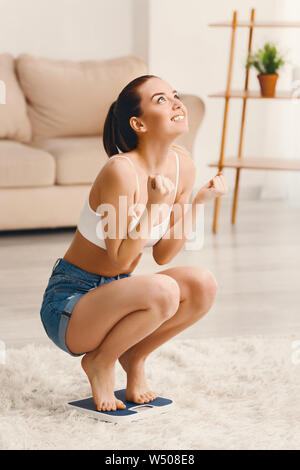 Glückliche junge Frau auf Waage zu Hause. Gewicht-verlust-Konzept Stockfoto