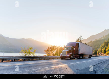 Big Rig klassische amerikanische Leistungsstarke braun Semi Truck mit kühlkoffer Auflieger für den Transport von tiefgekühlten Waren, die auf der Straße entlang der Eisenbahn und Riv Stockfoto