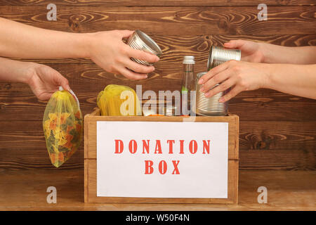 Freiwillige setzen Essen in die spendenbox auf hölzernen Hintergrund Stockfoto