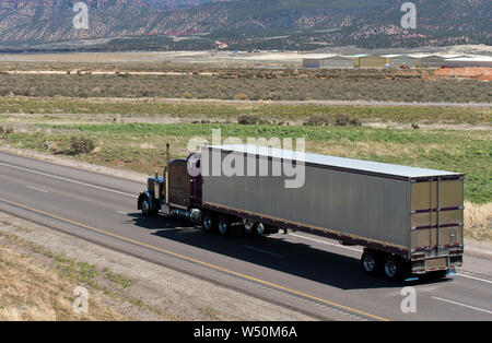 Dunkelbraun klassische amerikanische Motorhaube Long Haul Big Rig Semi Truck Transport gefroren kommerziellen Ladung in Aluminium kühlfahrzeug Auflieger auf dem Laufen Stockfoto