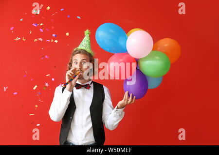 Junger Mann mit Geburtstag Ballons und Party Pfeifen auf farbigen Hintergrund Stockfoto