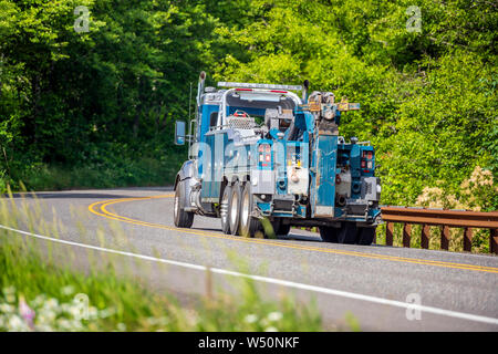 Leistungsstarke professionelle Blue Big Rig abschleppen Semi Truck für Tow semi Trucks, die auf den kurvenreichen Straße im grünen Wald für die Abholung ein defektes Fahrzeug, dass n Stockfoto