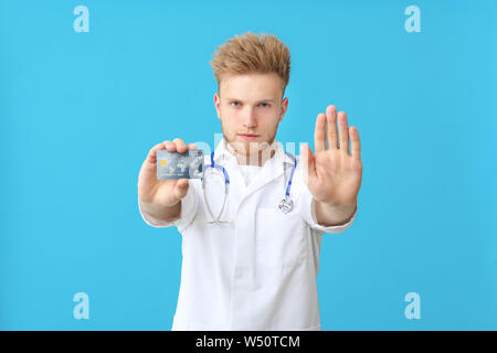 Männlicher Arzt mit Kreditkarte Übersicht stop Geste auf farbigen Hintergrund Stockfoto