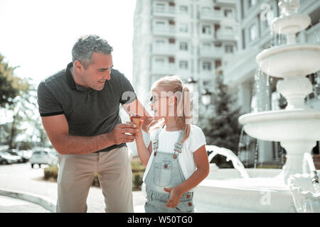 Vater - Tochter Zeit. Glücklichen kleinen Mädchen Schokolade essen Eis wandern mit ihrem Lächeln Vati ihr umarmte. Stockfoto