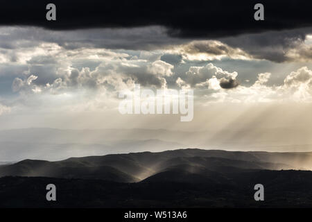 Sonnenstrahl scheint durch Wolken und Regen über die Berge in der Mitte der Schatten Stockfoto