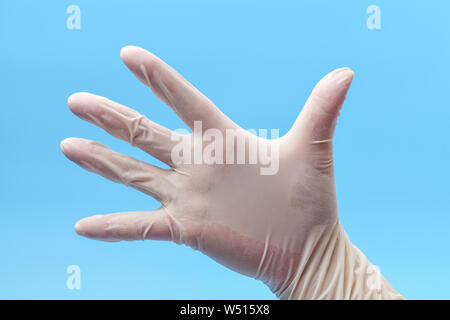 Durch das Tragen von schützender Hand oder OP-Handschuhe auf blauem Hintergrund. Hand in weißen Medizinische Handschuhe, in Stellung Öffnen Sie Palm. Medizinischen Hintergrund. Stockfoto