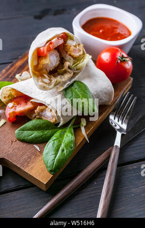 Nahaufnahme Tortilla Wraps mit gebratenen Garnelen, Salat und Tomaten auf einer hölzernen Schneidebrett. Gesundes Essen. Vertikaler Dampfstoß Stockfoto