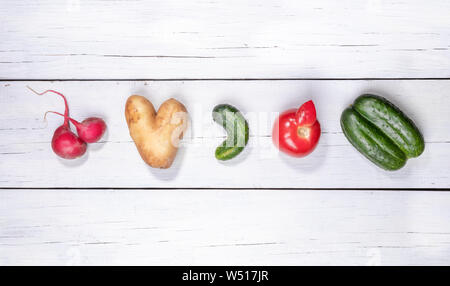 Satz von fünf hässliche Gemüse: Kartoffel, Tomate, Gurke und Radieschen, die in der Zeile festgelegt auf weißem Holz- Hintergrund. Stockfoto