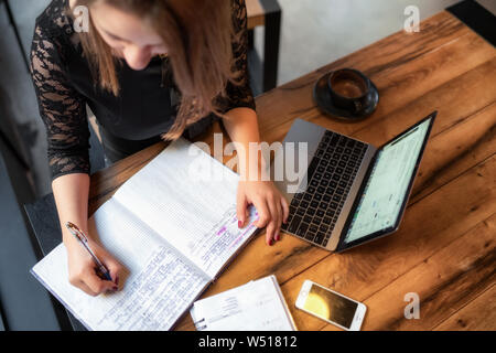 Brünette Frau am Tisch im Cafe mit Tasse heiße Schokolade Arbeiten am Laptop sitzen und schreiben im Notebook Stockfoto