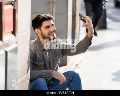 Aufgeregt trendige junge Mann unter selfie oder Blogging auf Smart Handy auf Reisen in europäischen Stadt Straße oder den Campus der Universität. Ferien und Techno Stockfoto