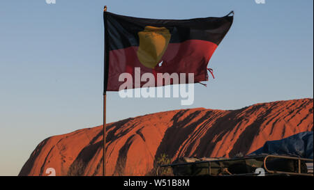 Die Aborigines Flagge vor ofUluru oder Ayers Rock im Zentrum Australiens. Die riesigen Monolith aus Sandstein ist heilig für Ureinwohner Australiens. Stockfoto