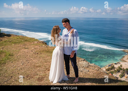 Der Mann und die Frau einander umarmen, stehend auf einer Klippe mit Blick auf das Meer an einem sonnigen Tag in Bali. Stockfoto