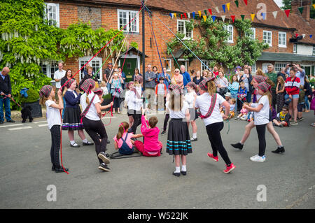Die Kinder der örtlichen Grundschule tanzen auf dem Dorfplatz in Yattendon, Bekshire, um den traditionellen Maibaum herum Stockfoto