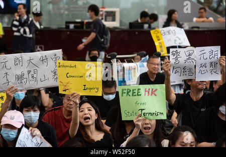 Prrotesters halten Plakate und Parolen während der im Protest am Flughafen Ankunft Halle sitzen. Hunderte von Demonstranten gegen die Regierung inszenierten einen Protest an der Hong Kong International Airport terminal Sitzen, das erste von drei geraden Tagen Demonstrationen nach Auseinandersetzungen in der vergangenen Woche ausgelöst wird befürchtet, dass eine breitere Auseinandersetzung in der Stadt ausbrechen könnte Stockfoto