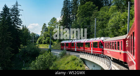 St. Peter, GR/Schweiz - 24. Juli, 2019: rot Schmalspurbahn über eine steinerne Brücke auf einer kurvenreichen Strecke in den Schweizer Alpen auf der Stockfoto