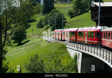 St. Peter, GR/Schweiz - 24. Juli, 2019: rot Schmalspurbahn über eine steinerne Brücke auf einer kurvenreichen Strecke in den Schweizer Alpen auf der Stockfoto