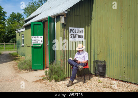 Ein Mann in einem Strohhut liest in der Sonne vor dem Wahllokal in South Stoke, Oxfordshire Stockfoto