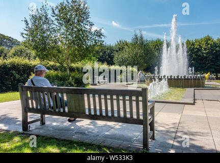 Ein Mann sitzt auf einer Parkbank am Jubiläum Brunnen in Goswell Park, Windsor, Berkshire, Großbritannien Stockfoto