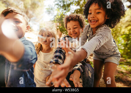 Gruppe der spielenden Kinder mit Seifenblasen im Wald. Junge bläst Seifenblasen mit Freunden, die versuchen, die Blasen zu fangen. Stockfoto