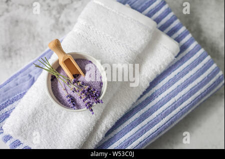 Stapel sauber weiche Handtücher mit einem Bündel von Lavendel und Badesalz auf hellgrauem Hintergrund. Wellness Handtücher gegen eine texturierte Wand. Minimalismus, weiche Schwerpunkte Stockfoto