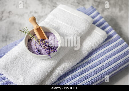 Stapel sauber weiche Handtücher mit einem Bündel von Lavendel und Badesalz auf hellgrauem Hintergrund. Wellness Handtücher gegen eine texturierte Wand. Minimalismus, weiche Schwerpunkte Stockfoto