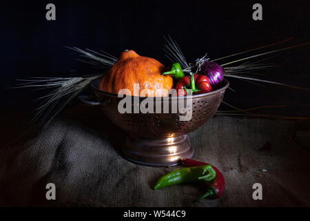 Noch immer leben auf einem schwarzen Hintergrund. Orange Kürbis, rote und grüne Paprika, lila Zwiebeln, getrocknet Weizen Ringe in einem Metall Schale Stockfoto