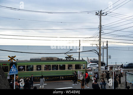 Touristen nehmen Fotos als einen Zug auf der Enoden Linie fährt hinter dem Bahnübergang gegen die Skyline von Sea Scape in Kamakura, Kanagawa, Japan, 2. Stockfoto