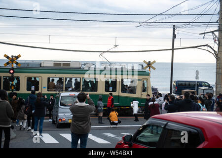 Touristen nehmen Fotos als einen Zug auf der Enoden Linie fährt hinter dem Bahnübergang gegen die Skyline von Sea Scape in Kamakura, Kanagawa, Japan, 2. Stockfoto
