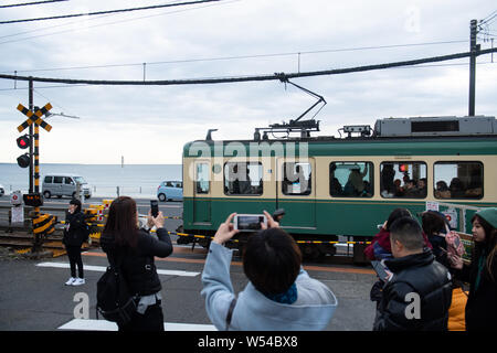 Touristen nehmen Fotos als einen Zug auf der Enoden Linie fährt hinter dem Bahnübergang gegen die Skyline von Sea Scape in Kamakura, Kanagawa, Japan, 2. Stockfoto