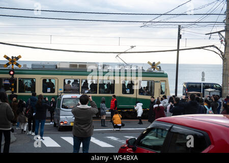 Touristen nehmen Fotos als einen Zug auf der Enoden Linie fährt hinter dem Bahnübergang gegen die Skyline von Sea Scape in Kamakura, Kanagawa, Japan, 2. Stockfoto