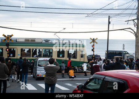 Touristen nehmen Fotos als einen Zug auf der Enoden Linie fährt hinter dem Bahnübergang gegen die Skyline von Sea Scape in Kamakura, Kanagawa, Japan, 2. Stockfoto