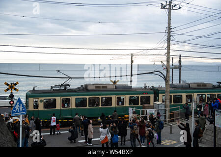 Touristen nehmen Fotos als einen Zug auf der Enoden Linie fährt hinter dem Bahnübergang gegen die Skyline von Sea Scape in Kamakura, Kanagawa, Japan, 2. Stockfoto