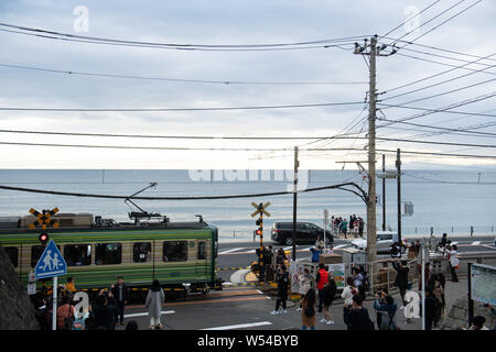 Touristen nehmen Fotos als einen Zug auf der Enoden Linie fährt hinter dem Bahnübergang gegen die Skyline von Sea Scape in Kamakura, Kanagawa, Japan, 2. Stockfoto