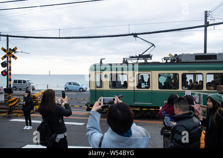 Touristen nehmen Fotos als einen Zug auf der Enoden Linie fährt hinter dem Bahnübergang gegen die Skyline von Sea Scape in Kamakura, Kanagawa, Japan, 2. Stockfoto