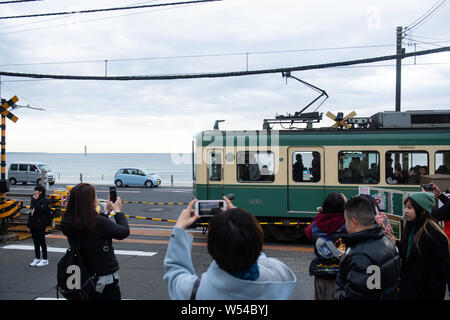Touristen nehmen Fotos als einen Zug auf der Enoden Linie fährt hinter dem Bahnübergang gegen die Skyline von Sea Scape in Kamakura, Kanagawa, Japan, 2. Stockfoto