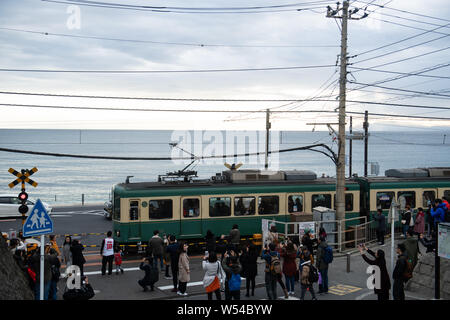 Touristen nehmen Fotos als einen Zug auf der Enoden Linie fährt hinter dem Bahnübergang gegen die Skyline von Sea Scape in Kamakura, Kanagawa, Japan, 2. Stockfoto