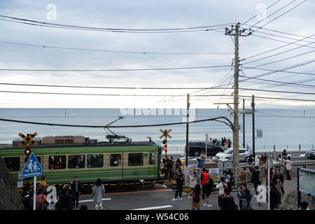 Touristen nehmen Fotos als einen Zug auf der Enoden Linie fährt hinter dem Bahnübergang gegen die Skyline von Sea Scape in Kamakura, Kanagawa, Japan, 2. Stockfoto