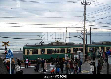 Touristen nehmen Fotos als einen Zug auf der Enoden Linie fährt hinter dem Bahnübergang gegen die Skyline von Sea Scape in Kamakura, Kanagawa, Japan, 2. Stockfoto