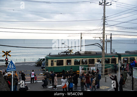 Touristen nehmen Fotos als einen Zug auf der Enoden Linie fährt hinter dem Bahnübergang gegen die Skyline von Sea Scape in Kamakura, Kanagawa, Japan, 2. Stockfoto