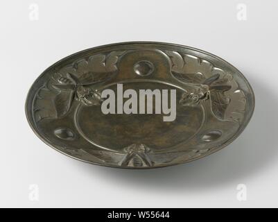 Schüssel mit fliegenden Hirsche in der Entlastung, der angetriebenen Schüssel ist mit einem Schmuck aus einem Stempel Form gestanzt, bestehend aus drei flying Hirsch mit gespreizte Flügel, in Richtung der Kante, die durch stilisierte Geweihe und granulierte Oberfläche Abschnitte miteinander verbunden. Diese Dekoration ist mit drei unbearbeitete Flächen mit einer glatten, flachen ball Stud in der Mitte und welche ausgeschaltet sind durch eine Rippe geschlossen durchsetzt. Das Gericht hat eine verdickte Rand und wird auf eine runde Grundfläche, in der zwei Bohrungen für die Platzierung an der Wand gemacht werden platziert., G. Dikkers & Co, C. 1905, Messing (Legierung), Körnung, h 5,8 cm x T 36,2 cm x T 11 cm Stockfoto