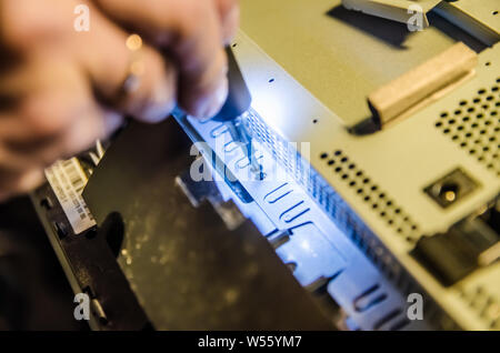 Mann unspins die Abdeckung des Steuergeräts der Monoblock mit einem Schraubendreher mit Hintergrundbeleuchtung Stockfoto