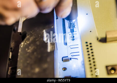 Mann unspins die Abdeckung des Steuergeräts der Monoblock mit einem Schraubendreher mit Hintergrundbeleuchtung Stockfoto