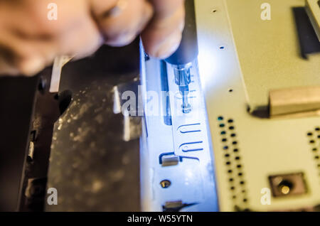 Mann unspins die Abdeckung des Steuergeräts der Monoblock mit einem Schraubendreher mit Hintergrundbeleuchtung Stockfoto