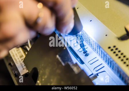 Mann unspins die Abdeckung des Steuergeräts der Monoblock mit einem Schraubendreher mit Hintergrundbeleuchtung Stockfoto