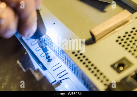 Mann unspins die Abdeckung des Steuergeräts der Monoblock mit einem Schraubendreher mit Hintergrundbeleuchtung Stockfoto